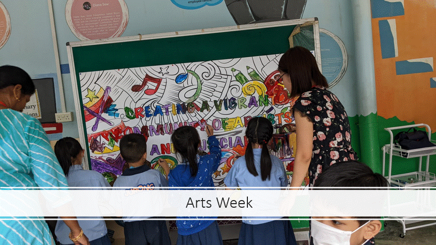 Children and a teacher collaborate on a colorful mural board during Arts Week at school.